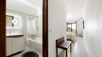 A modern bathroom with a bathtub, a vanity with a mirror, and a bench in a hallway.