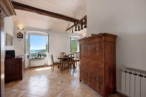 Un espace repas comprenant une table et des chaises en bois, un grand meuble en bois et une vue dégagée sur l’extérieur grâce à une arche ouverte.