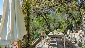 An outdoor patio with a table and chairs, surrounded by greenery and stone walls.