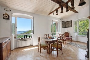 Un coin repas comprenant une table, des chaises, une vue par la fenêtre, une horloge et un mur en pierre.