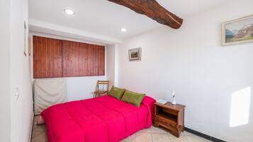 A bedroom with a red bed, wooden headboard, a nightstand, a chair, and a painting on the wall.