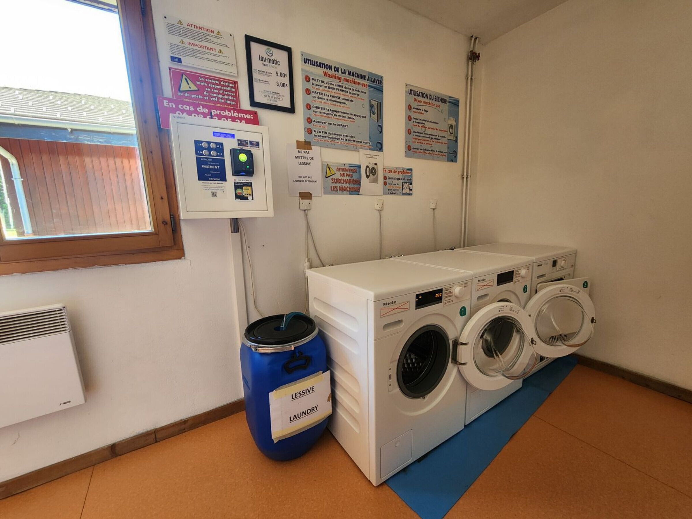 Une buanderie équipée d’un lave-linge, d’un sèche-linge et d’une poubelle bleue portant l’inscription « PRODUITS DE LESSIVE ».