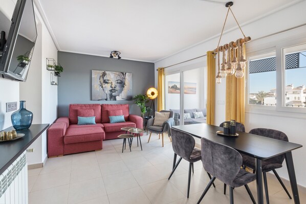 A modern living room with a red sofa, a dining table, and a large window with curtains.