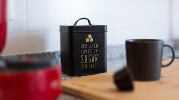 Uma bancada de cozinha com um recipiente preto, um eletrodoméstico vermelho e uma caneca preta.
