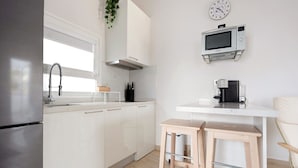 Una cocina moderna con armarios blancos, un refrigerador de acero inoxidable, un microondas y una máquina de café.