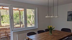 En matplats med ett träbord och stolar, stora fönster med utsikt över träd och hängande lampor.