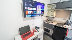 A modern kitchen with a flat-screen TV mounted on the wall, a laptop on a desk, and a compact refrigerator. - Spacious Studio Near City Centre! (Birmingham)