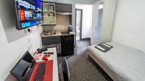 A compact room with a kitchenette, a bed, a desk with a laptop, and a TV displaying streaming services. - Spacious Studio Near City Centre! (Birmingham)