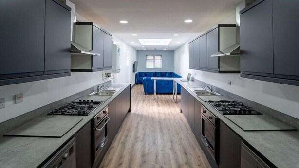 A modern kitchen with grey cabinets, a central island, and a blue sofa in the background. - Spacious Studio Near City Centre! (Birmingham)