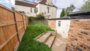A narrow backyard with a wooden fence, a grassy area, and a small brick wall with steps leading to a door. - Spacious Studio Near City Centre! (Birmingham)