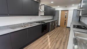 A modern kitchen with grey cabinets, a stainless steel range hood, a built-in oven, and a washing machine.