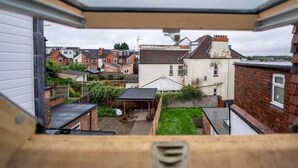 A view from a window overlooking a residential area with houses, a small garden, and a brick wall.