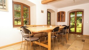 Un comedor con mesa y sillas de madera, ventanas amplias y vista a zonas verdes.