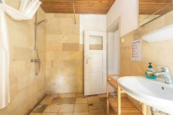 Un baño con ducha, lavamanos y estante de madera.