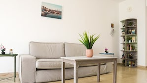 Ein Wohnzimmer mit einer Couch, einem Couchtisch, einem Bücherregal und einer Zimmerpflanze.