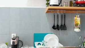 Eine kompakte Küche mit Geschirrspüler, Kaffeemaschine, Wasserkocher und Spüle. Küchenutensilien hängen an der Wand und eine kleine Pflanze steht auf dem Regal.