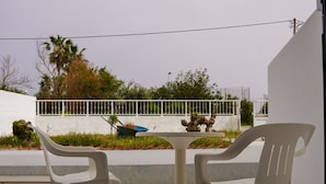 Eine Terrasse mit zwei weißen Plastikstühlen, einem kleinen Tisch und einem Rasenwagen.