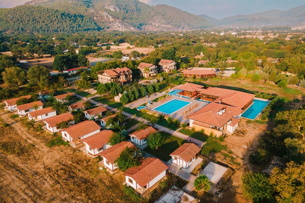 An aerial view of a resort with multiple villas, a central pool area, and surrounding greenery.