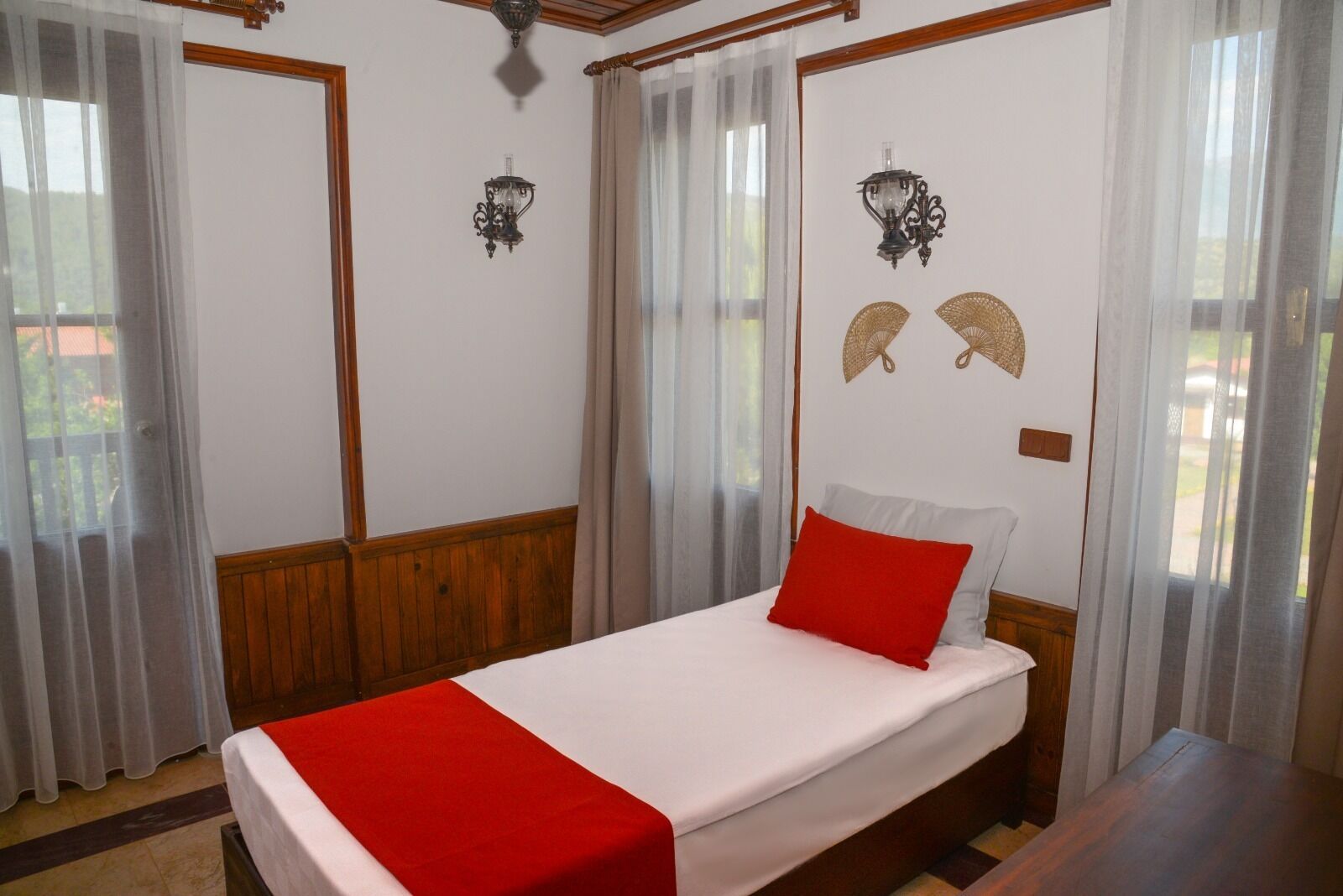A bedroom with a bed, wooden paneling, two wall-mounted lamps, and sheer curtains.