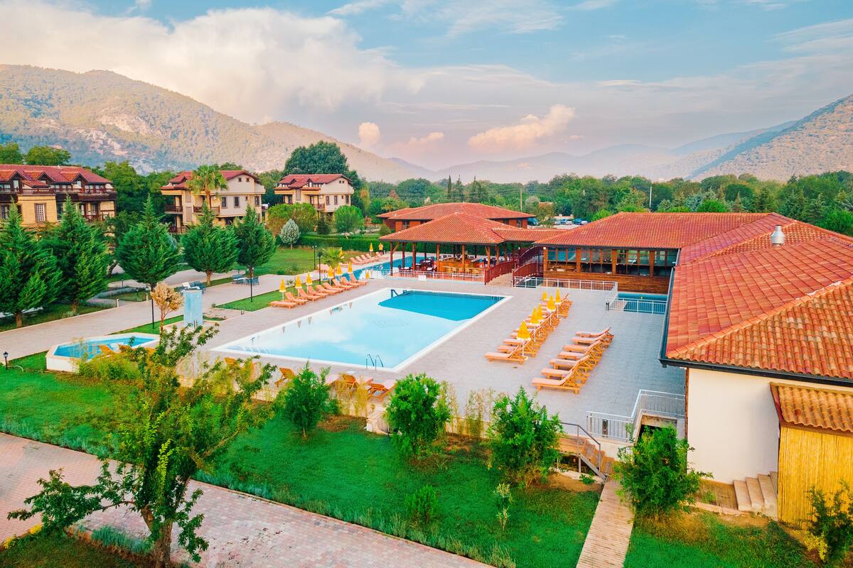 A resort with a swimming pool, sun loungers, and a view of mountains.