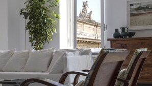 A living room with a sofa, chairs, a plant, a window with a view of a statue, and a wooden cabinet with decorative items. - GuestHost - Large and bright 200sqm apartment, able to accommodate up to 7 people, located on the 3rd floor with elevator (not suitable for disabled people) of a building dating back to the 19th century. The property overlooks Piazza Fanti's garden and i (Roma)