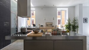 A modern kitchen with a central island, stainless steel appliances, and a chalkboard with writing. - GuestHost - Large and bright 200sqm apartment, able to accommodate up to 7 people, located on the 3rd floor with elevator (not suitable for disabled people) of a building dating back to the 19th century. The property overlooks Piazza Fanti's garden and i (Roma)