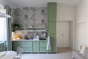 A compact kitchen with a green cabinet, a white countertop, and a marble backsplash.