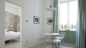 A room with a bed, a dining table with chairs, a hanging light fixture, and a window with curtains.