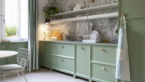 A kitchen with a green color scheme, white cabinets, a white chair, and a window with curtains.