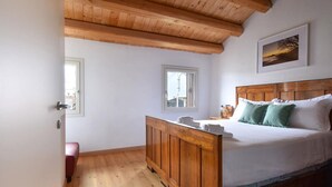 Ein Schlafzimmer mit einem hölzernen Kopfende, einem Bett mit weißer Bettwäsche, einer Holzkommode und zwei Fenstern.