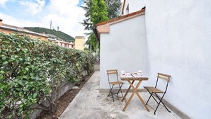 Eine Terrasse mit Tisch und Stühlen, einer weißen Wand und einer Hecke.