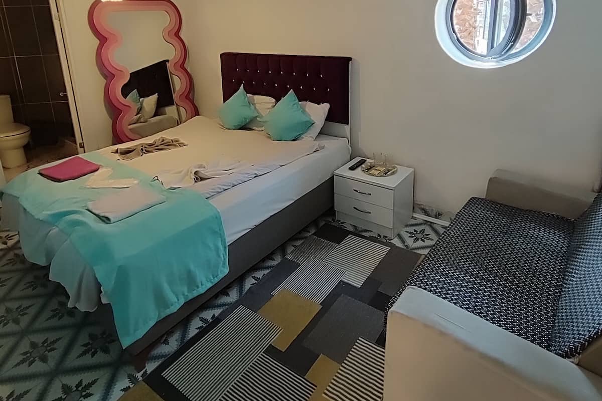 Quarto com cama, mesa de cabeceira e uma janela redonda.