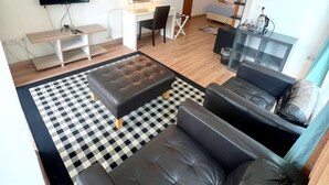Ett modernt vardagsrum med en svart lädersoffa, en svartvit rutig matta, en tv, en sminkbord med spegel och en hänglampa.