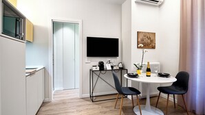 A modern kitchen with a built-in microwave, a dining area with a round table and two chairs, a flat-screen TV mounted on the wall, and a radiator under the window. - Yellow Donatello Charming suite by Hospity (Milano)