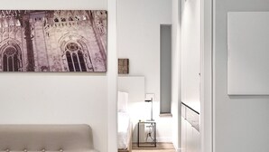 A modern hotel room with a wooden floor, a beige sofa, a painting of a building, and a suitcase in the background. - Yellow Donatello Charming suite by Hospity (Milano)