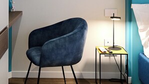 A modern room with a blue armchair, a small side table with a lamp, and a wall-mounted picture of a fashion runway.