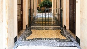 A corridor with a tiled floor, a metal railing, and a plant in the distance.