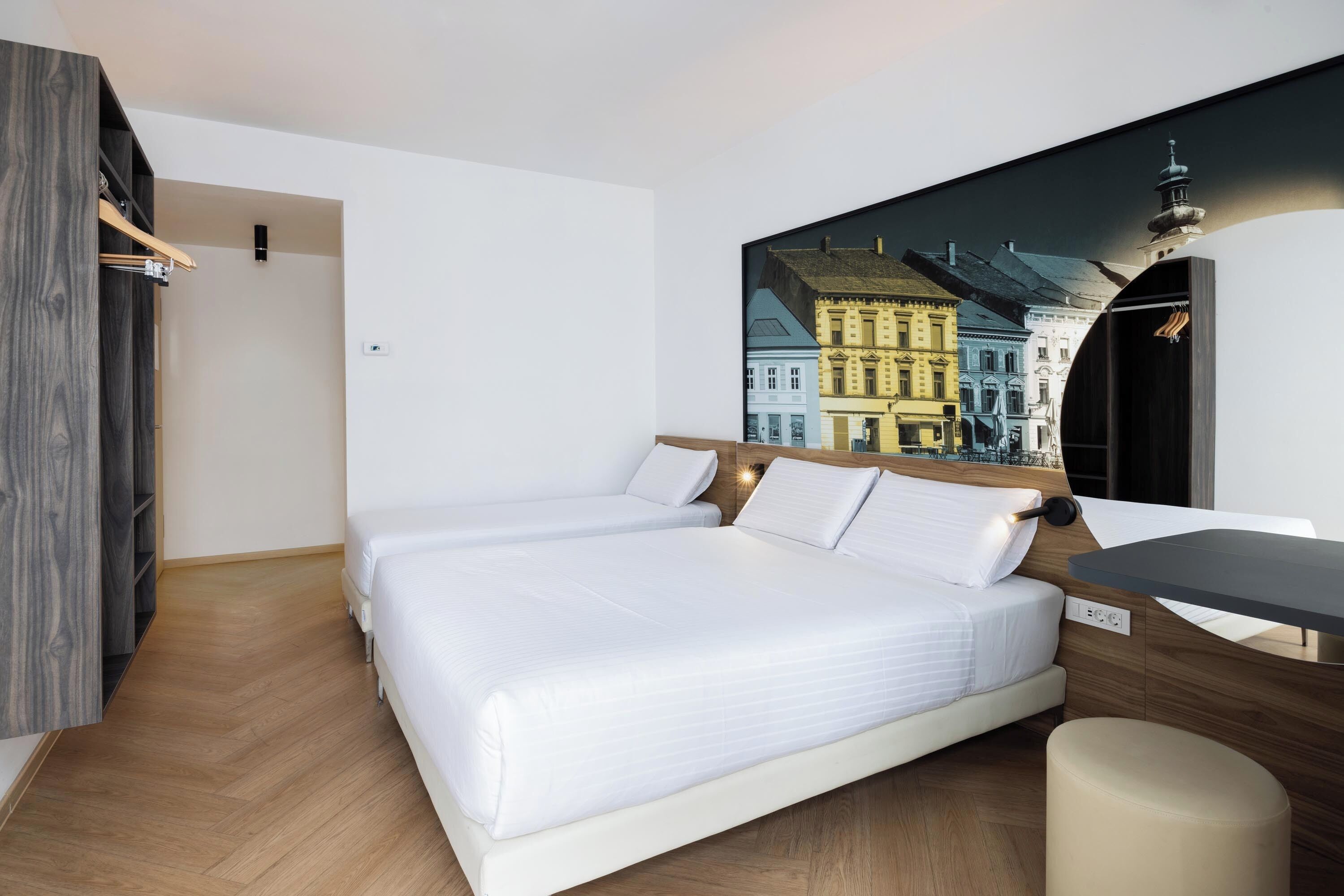 A hotel room with a large bed, a desk, and a wall-mounted TV displaying a cityscape.