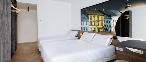 A hotel room with a large bed, a desk, and a wall-mounted TV displaying a cityscape.