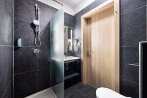 Un baño moderno con cabina de ducha de vidrio, puerta de madera y un inodoro blanco.