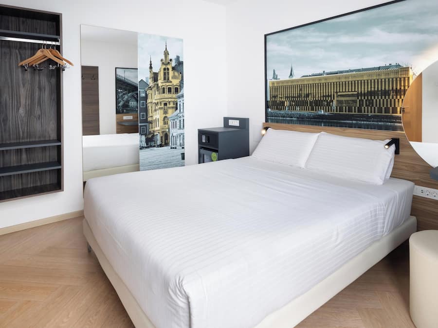 Una camera d'albergo con un letto grande, un armadio in legno, una scrivania con una sedia e due televisori a parete.