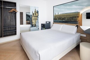 Habitación de hotel con una cama grande, un armario de madera, un escritorio con una silla y dos televisores montados en la pared.