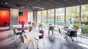 An indoor dining area with tables and chairs, large windows, and a red accent wall. - B&B Hotel Maribor (Maribor)