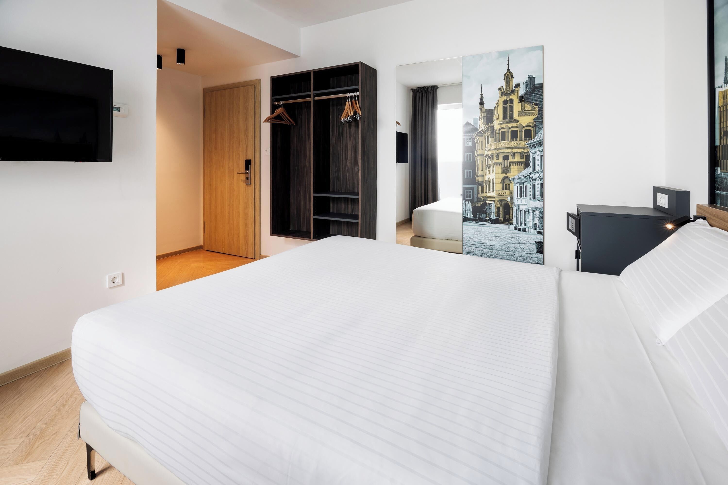 A hotel room with a large bed, a wardrobe, a mirror, and a television.