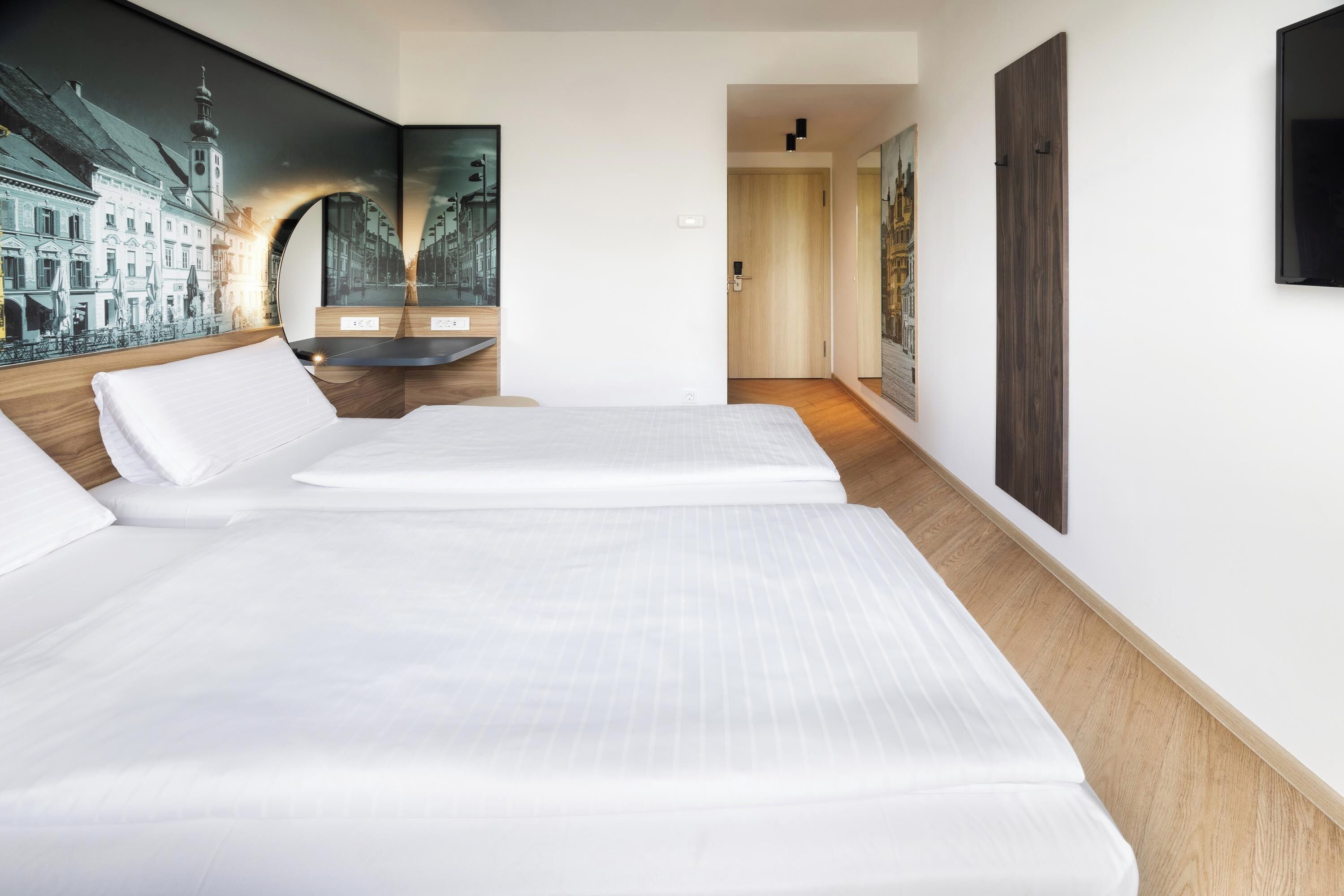 A hotel room with two beds, a large wall mural, and a wooden floor.