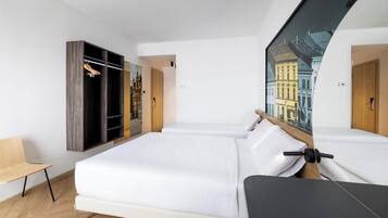 Ein modernes Hotelzimmer mit einem großen Bett, einer hölzernen Sitzbank, einem Schrank mit Spiegel und Blick auf die Stadt.