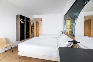 Habitación de hotel moderna con una cama grande, un banco de madera, un armario con espejo y vistas a un paisaje urbano.