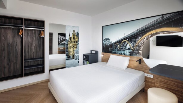 A modern hotel room with a large bed, a wardrobe, a desk, and a large wall-mounted TV. - B&B Hotel Maribor (Maribor)