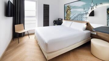 Una habitación de hotel con cama, escritorio, silla, televisor y un cuadro de un paisaje urbano.