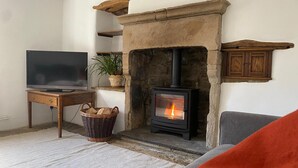 A living room with a stone fireplace, a television on a wooden stand, a wicker basket, and a grey sofa. - Beautiful Peak District Cottage With Hot Tub (Hope Valley)